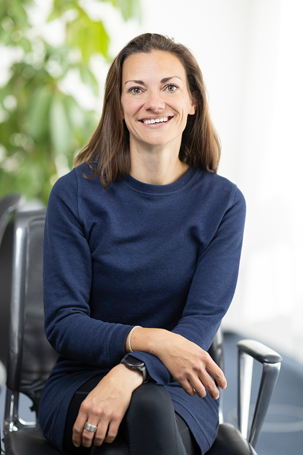Insolvenzbuchhaltung bei der MIZ. Eine lächelnde Frau sitzt auf einem Stuhl, trägt ein dunkelblaues Kleid.