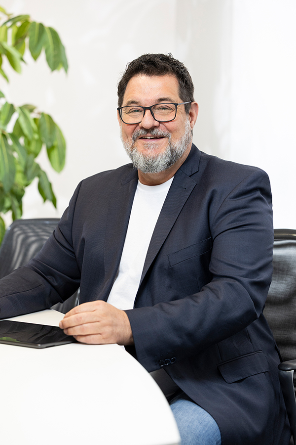 Prüfungsassistent der MIZ sitzt in einem Büro, trägt ein Sakko und hält ein Tablet.