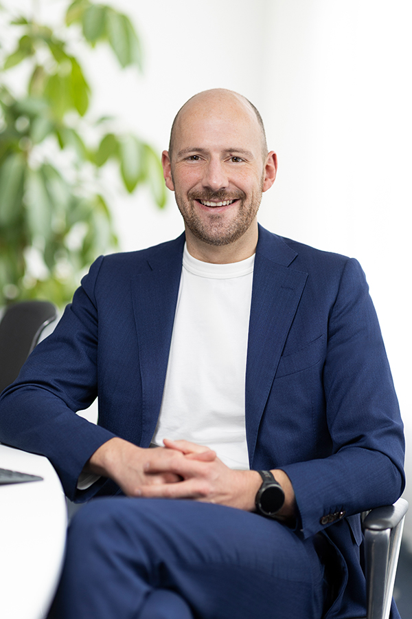Steuerberater bei MIZ. Ein Mann in einem blauen Anzug lächelt, sitzt an einem Tisch.